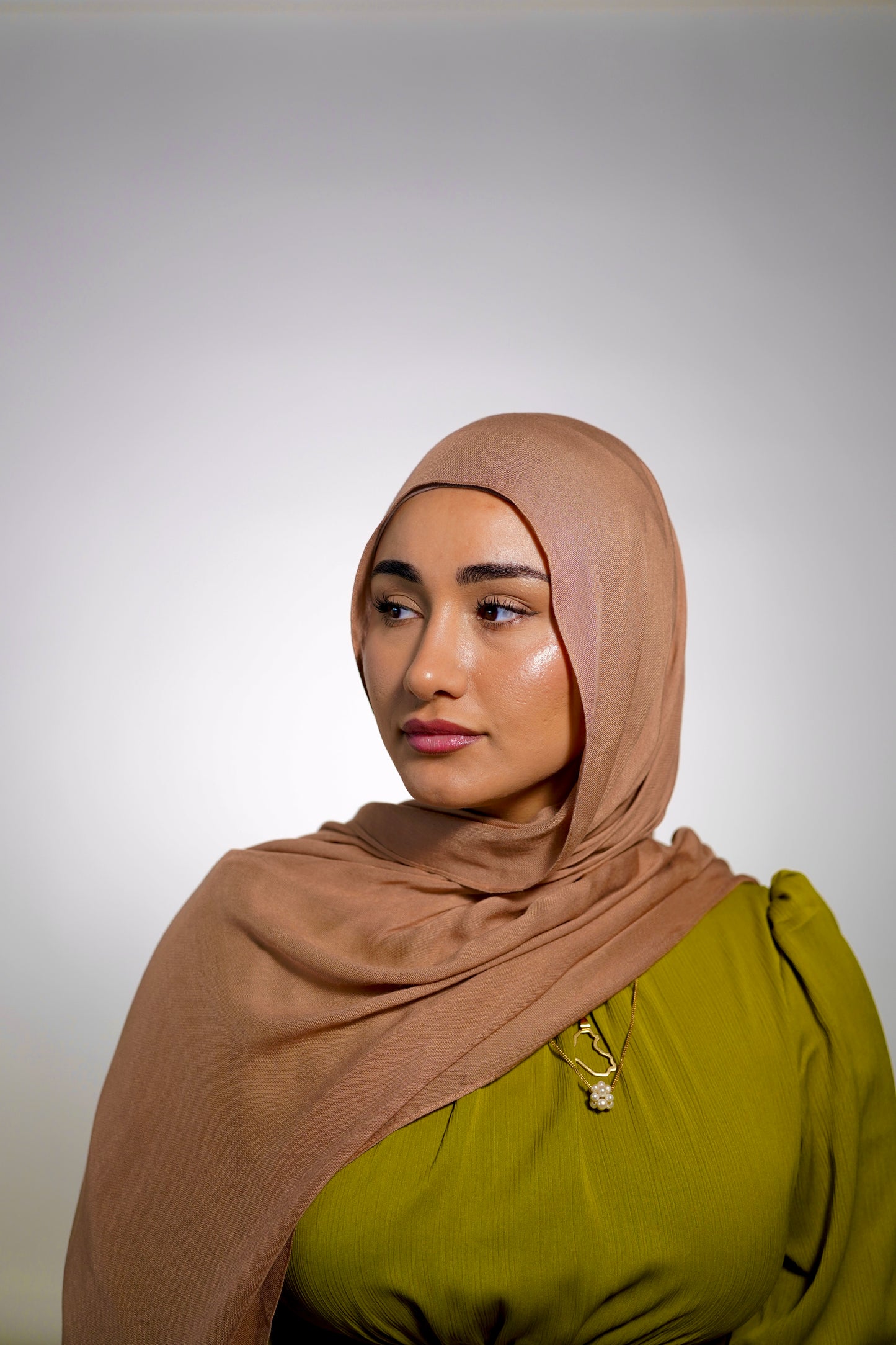 Hijabi women wearing a brown hijab in the color dunes and green modest dress by the brand malika the collection 
